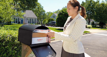 Young woman putting mail into a large black mailbox.